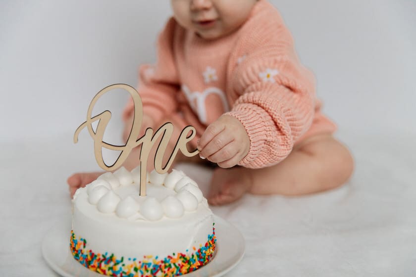 First birthday cake smash photo with a baby in pink sweater and a white birthday cake