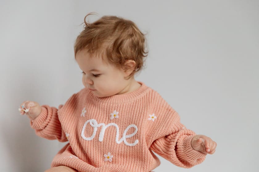 Baby in a pink sweater with One embroidered on the front