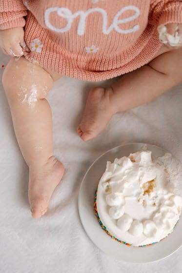 First birthday cake smash photo with a baby in pink sweater and a white birthday cake