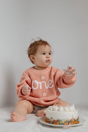 Baby on their first birthday playing with a white birthday cake