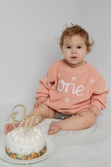 Little girl sitting with her first birthday cake looking at the camera