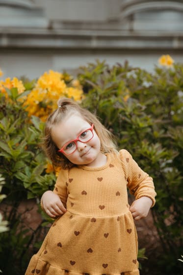 Young girl posing in a yellow dress with heart polka-dots and red glasses
