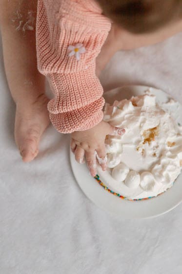 First birthday cake smash photo with a baby in pink sweater and a white birthday cake
