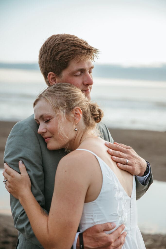 A bride and groom embracing on the beach after their backyard wedding