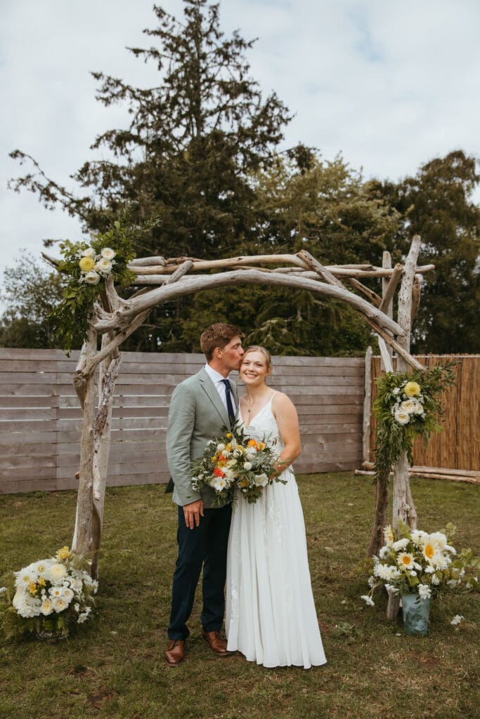 Bride and groom standing under a driftwood arch